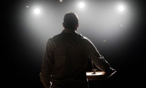 rear view of male professional speaker on stage under the spotlight