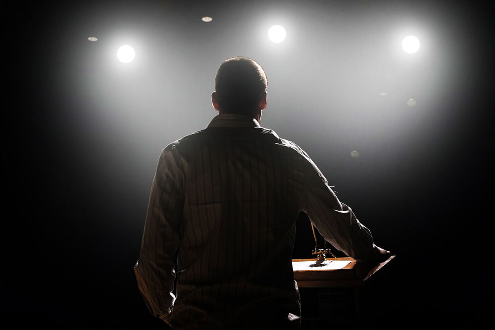 rear view of male professional speaker on stage under the spotlight