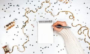 Ladies hand writing new year resolutions on pad surrounded by tinsel and glitter stars