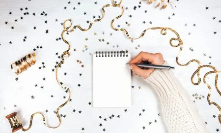 Ladies hand writing new year resolutions on pad surrounded by tinsel and glitter stars