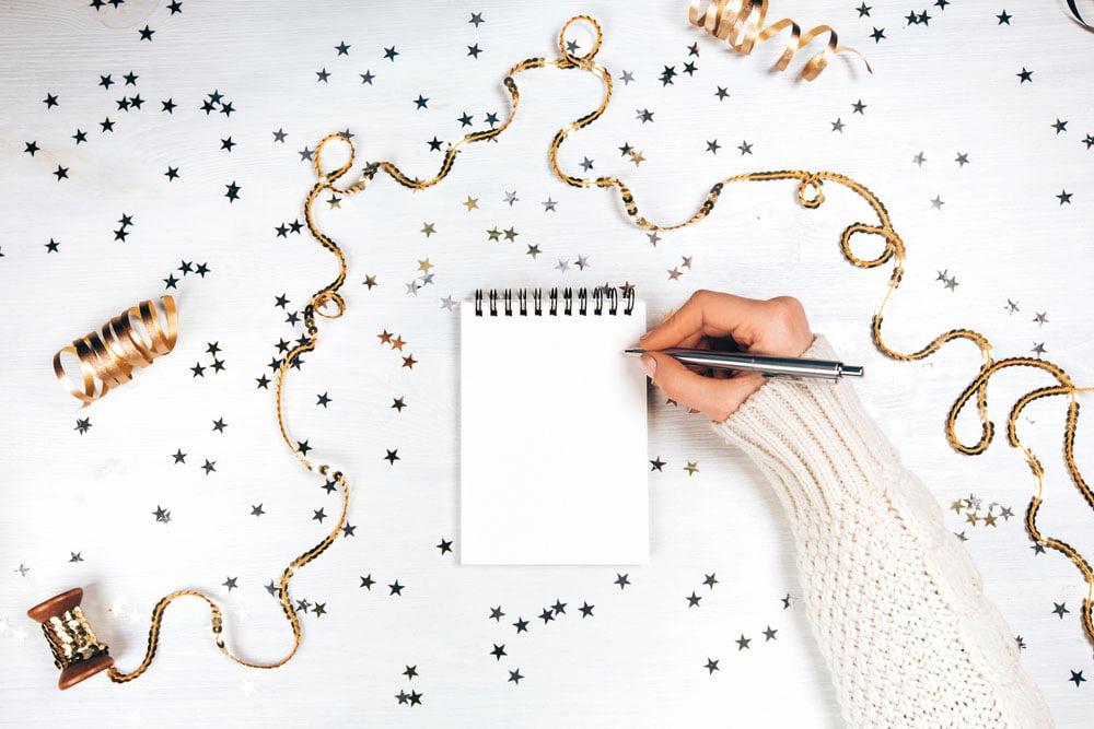 Ladies hand writing new year resolutions on pad surrounded by tinsel and glitter stars