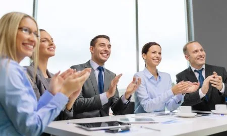 Smiling business people sat around table clapping successful impromptu speech