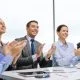 Smiling business people sat around table clapping successful impromptu speech