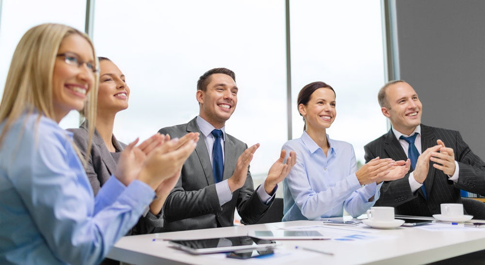 Smiling business people sat around table clapping successful impromptu speech