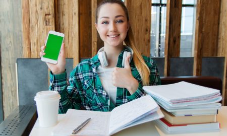 young student with large pile of books doing homework while listening to podcasts