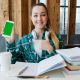 young student with large pile of books doing homework while listening to podcasts