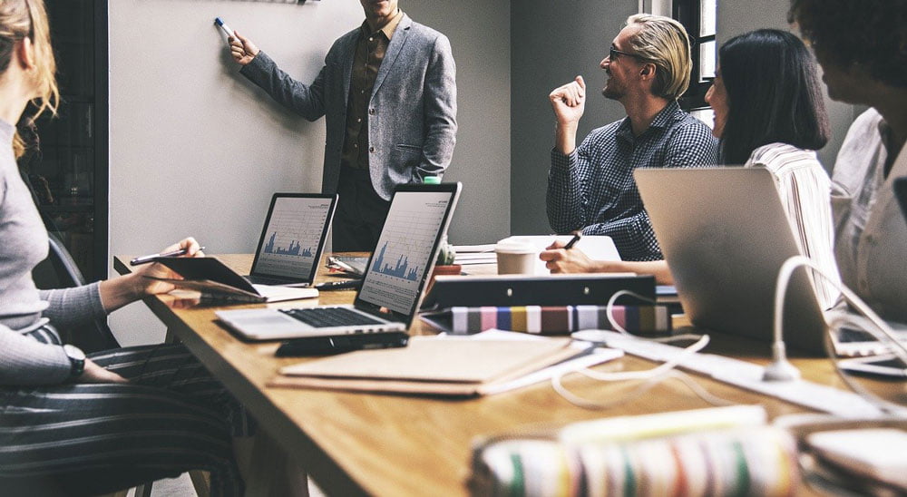 male presenter standing by screen in front of millennial business audience