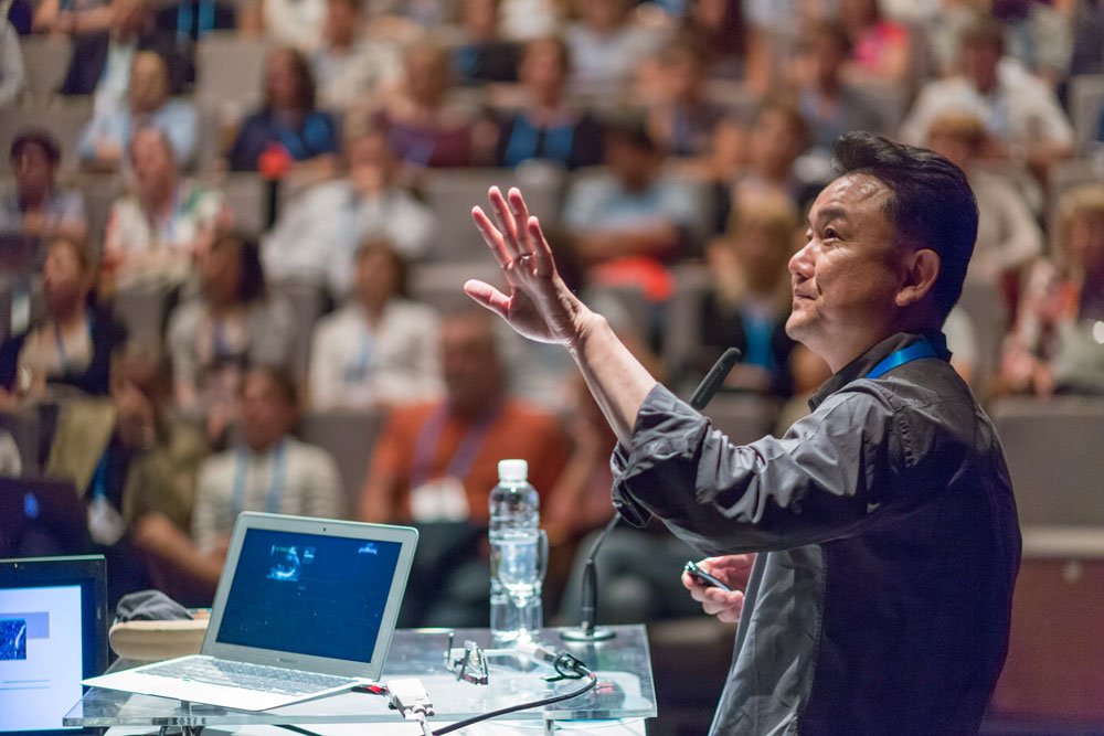 male presenter addressing large audience at scientific conference